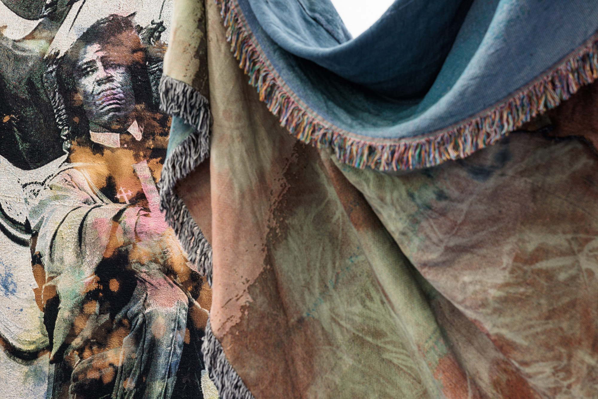 A close up of large, draped tapestries. The tapestry in the background has an image of James Brown. The tapestry in the front has a visible fringe around the edge. 