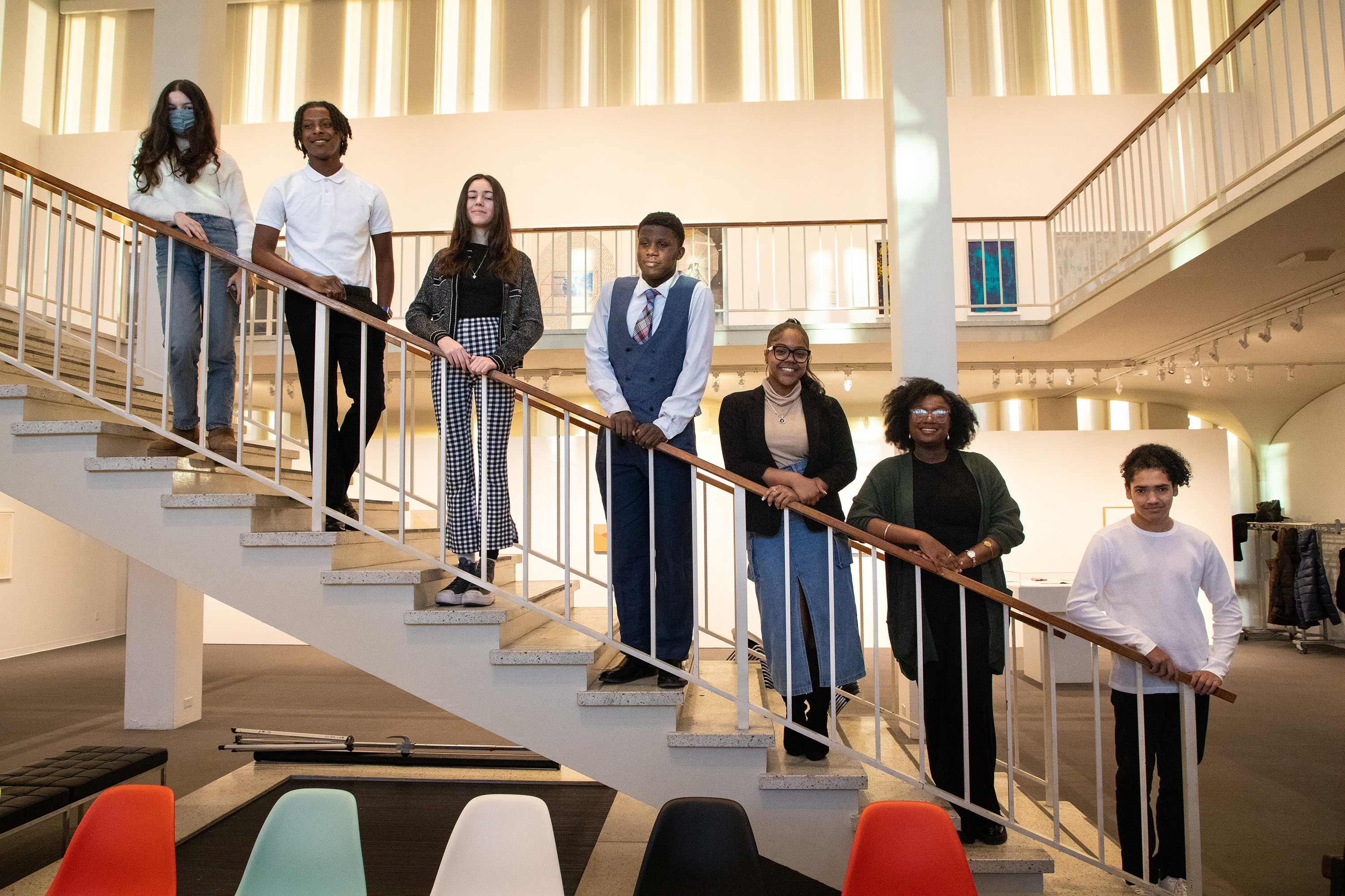 Seven high school students standing on the museum’s staircase. Each student is standing on a single step, creating a diagonal line. 