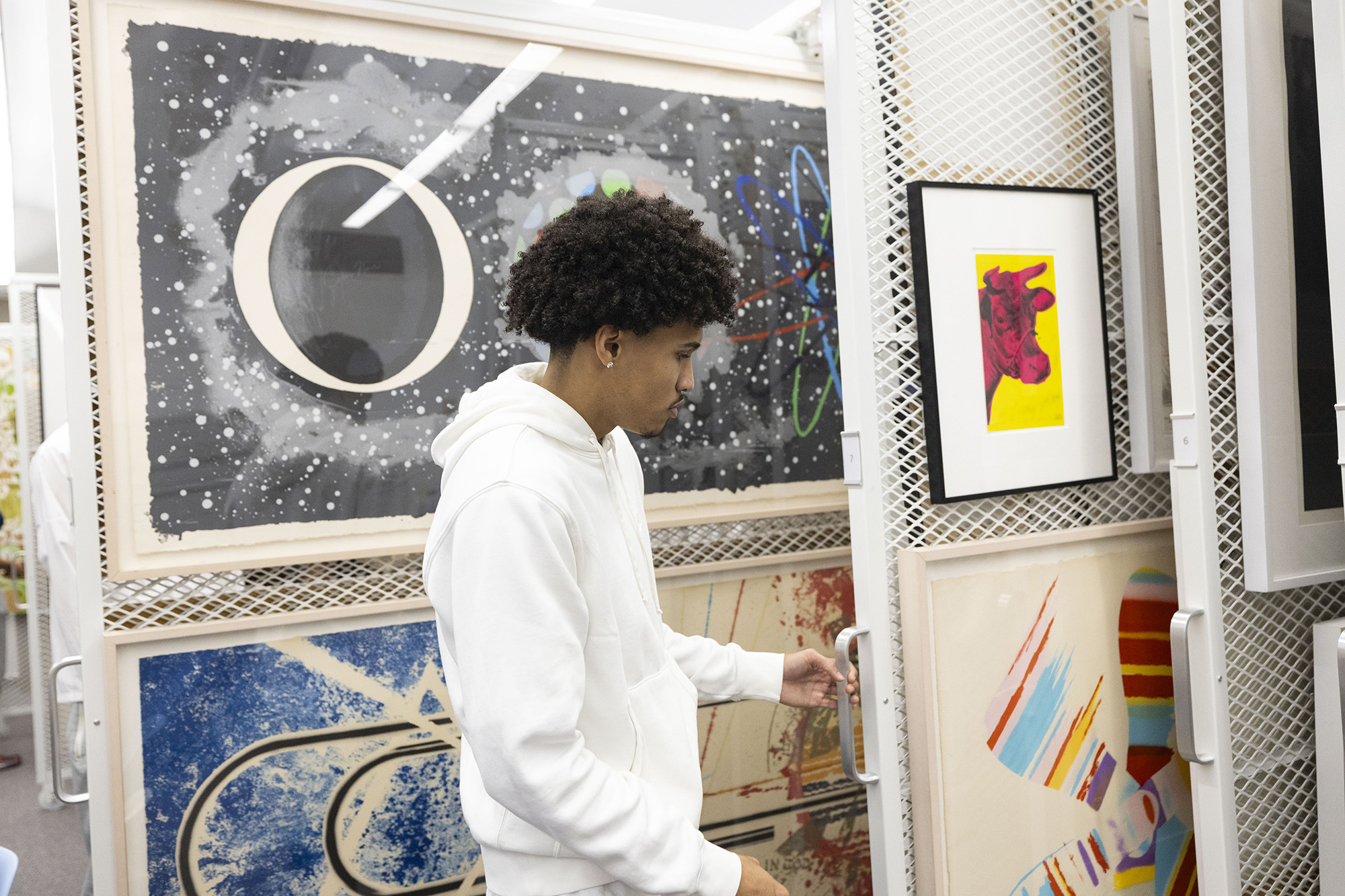 A student pulls out a sliding rack with framed artwork on it.