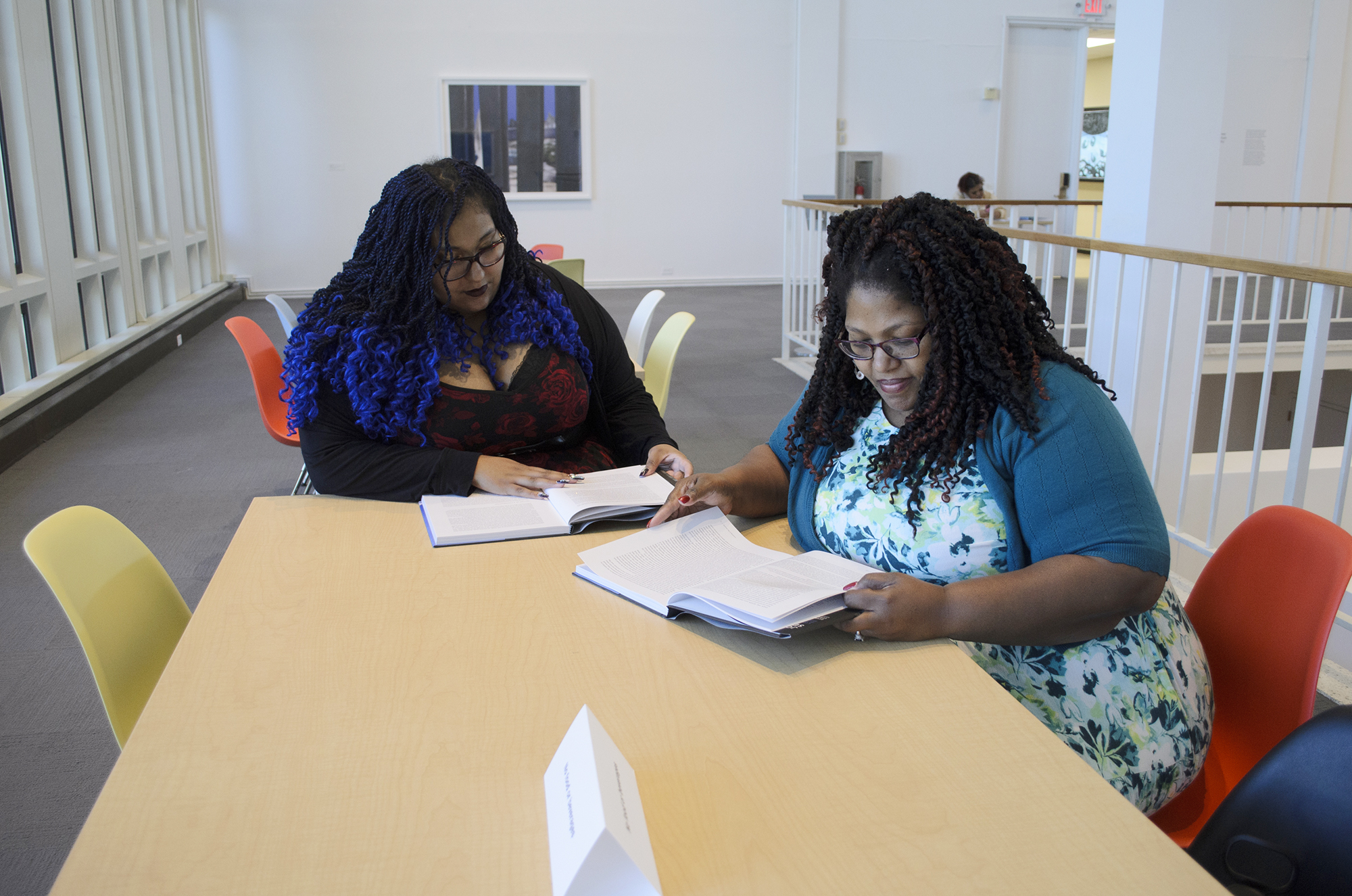 Two women seated at a table in the museum reading books.