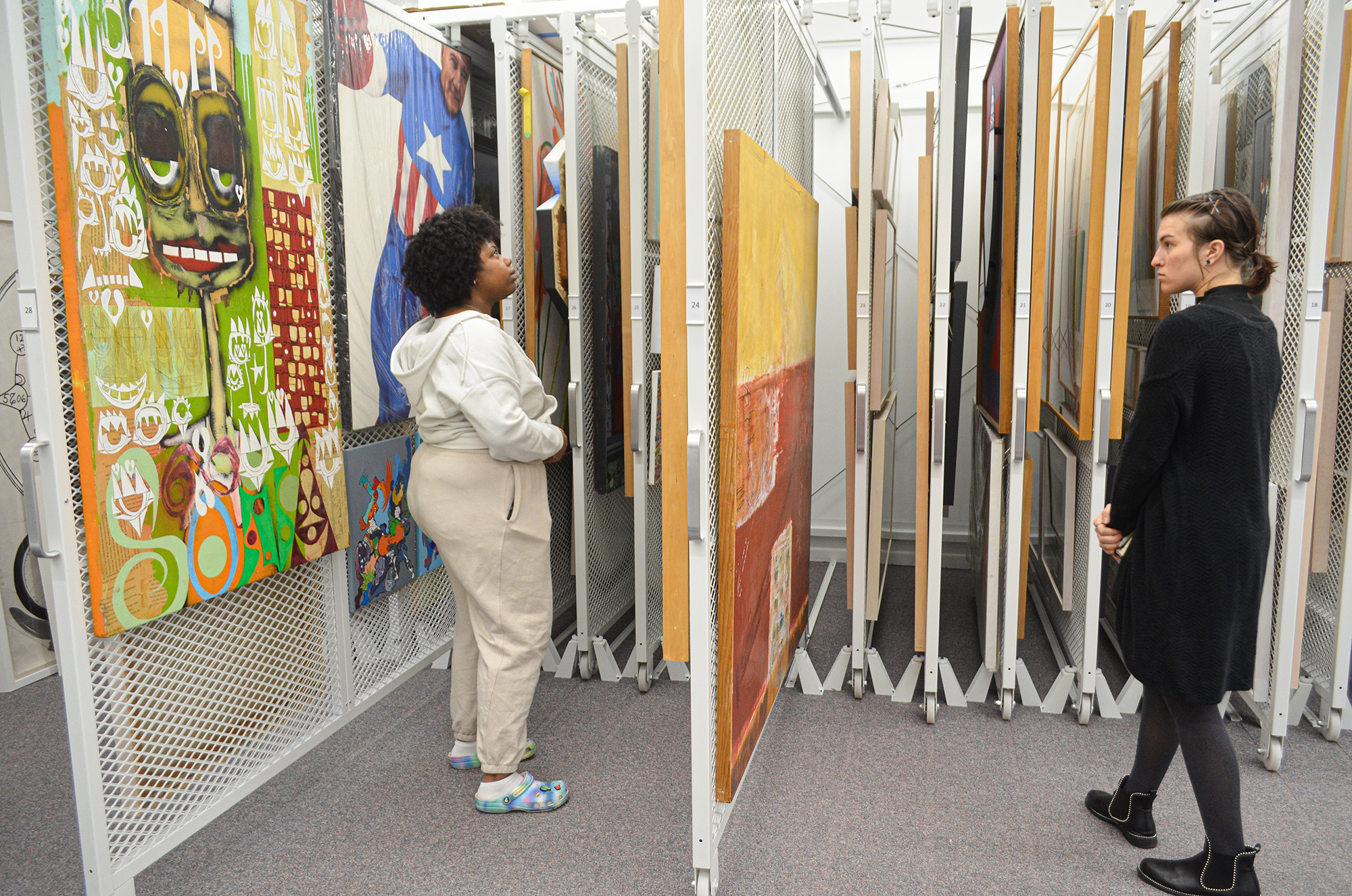 Two students looking at artwork on sliding racks. The students are facing each other, and a sliding rack is pulled out in between them.