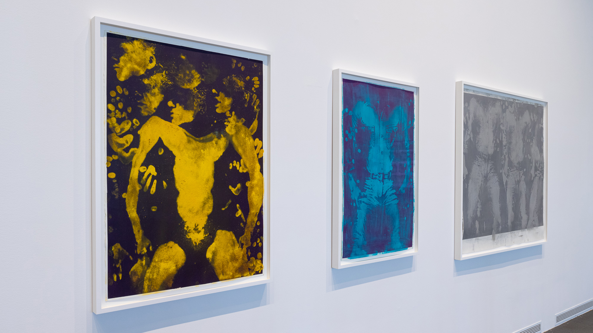 Angled image of three framed prints of bodies. The first is in yellow and black, the second features shades of blue, and the third includes shades of gray.