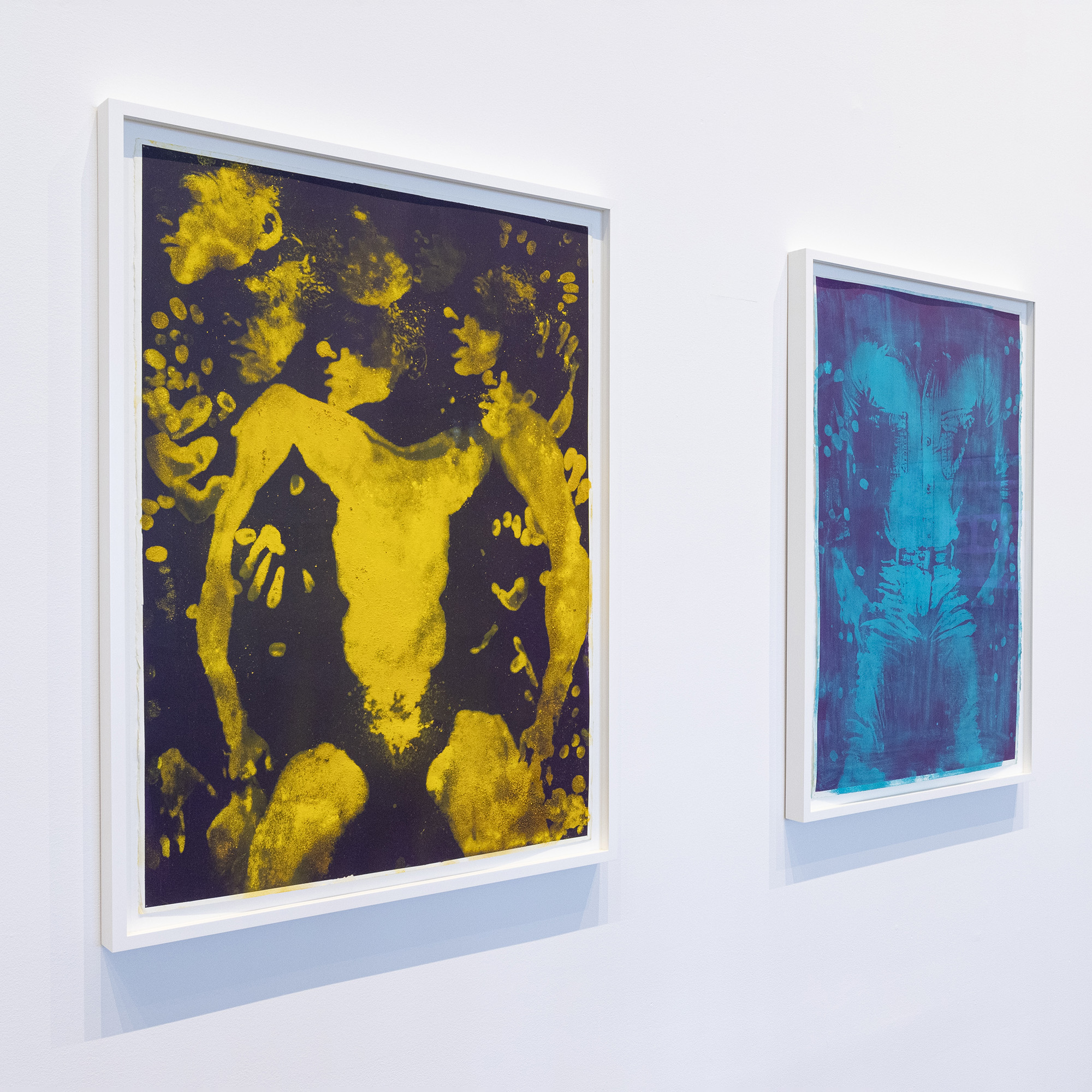 Angled image of three framed prints of bodies. The first is in yellow and black, the second features shades of blue, and the third includes shades of gray.